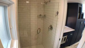 A bathroom with white subway tiles, a glass shower enclosure, and a dark-colored cabinet with a countertop.
