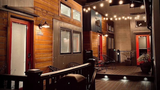 A cozy, well-lit indoor space with wooden walls and a wooden deck. There are several seating areas with chairs and tables, and a sign indicating a 'Hotel' on the left.