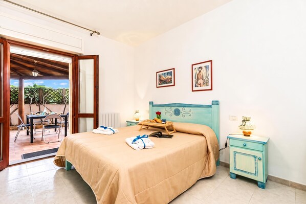 A hotel room with a bed, a table with breakfast, a chair, a window, and a door leading to an outdoor area.