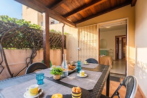 A covered outdoor dining area with a table set for breakfast, including croissants and a bottle.
