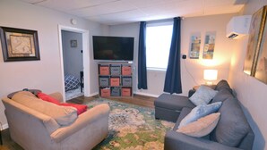 Una sala de estar con dos sofás, un televisor de pantalla plana, un tapete estampado y una ventana con cortinas.
