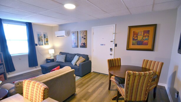 Una sala de estar amoblada con sofá, sillones, una mesa de comedor y un cuadro en la pared.