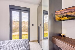 Une chambre à coucher moderne, avec un lit, un téléviseur fixé au mur et une porte-fenêtre coulissante donnant sur un balcon.