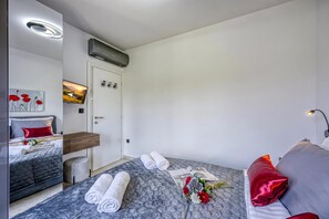 A modern hotel room with a bed, a desk, a chair, and a flat-screen TV.