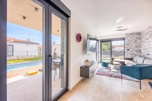 A modern living room with a pool view, a flat-screen TV, and a grey sofa. - Villa Gigi with private Pool, Višnjan, Croatia (Višnjan)
