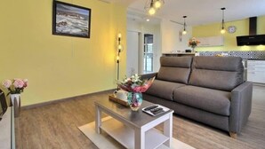 A living room with a sofa, a coffee table with a vase of flowers, and a painting on the wall. - La Maison Bleue - Comfortable appt Gr34 (Locmaria-Plouzané)