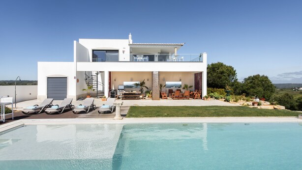 Una casa moderna de dos pisos con piscina, mobiliario exterior y vista al paisaje.