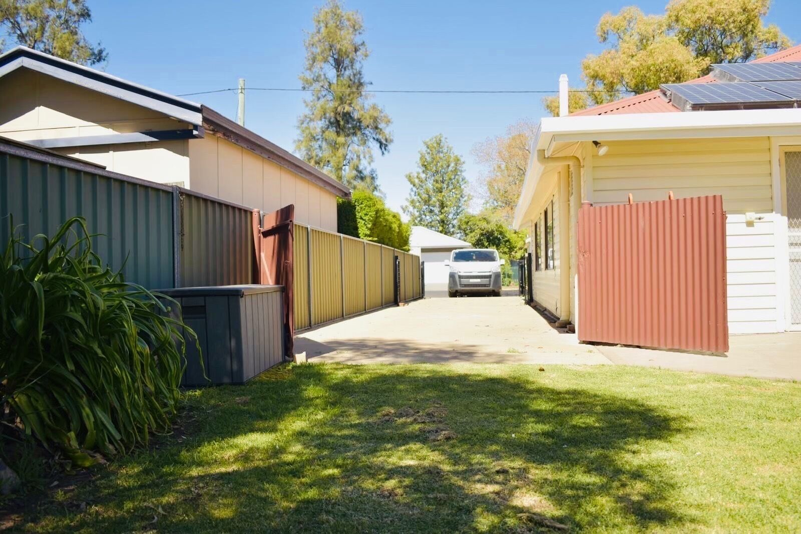 A residential street with houses on either side, a car parked in the driveway, and a clear sky.