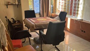 A dining area with a table set for four, surrounded by chairs, a small table with a chair, and a shelf with items. - Shengtang Business Hotel (Johannesburg)