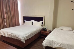 Habitación de hotel con dos camas, piso de madera, una mesita de noche con teléfono y lámpara, y una ventana con cortinas.