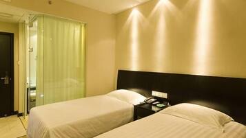 Een hotelkamer met twee bedden, een nachtkastje, een spiegel en een deur naar een badkamer.