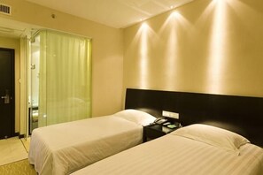 Habitación de hotel con dos camas, una mesita de noche, un espejo y una puerta que da al baño.