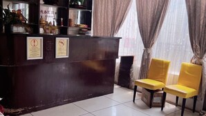 A reception area with a dark wooden desk, two yellow chairs, and a tiled floor. - Shengtang Business Hotel (Johannesburg)