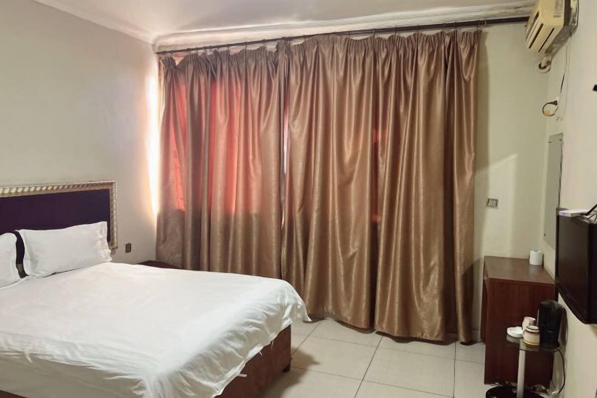 Ein Hotelzimmer mit Bett, Vorhängen, einem Fernseher und einem kleinen Tisch.