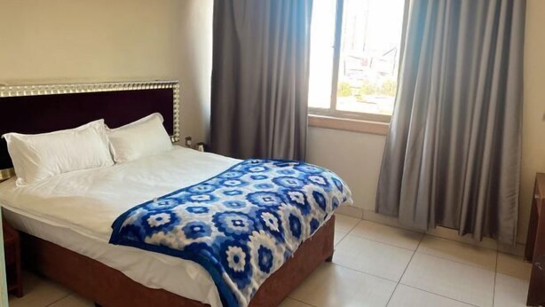 A bed with a patterned bedspread, a headboard, and curtains on a window. - Shengtang Business Hotel (Johannesburg)