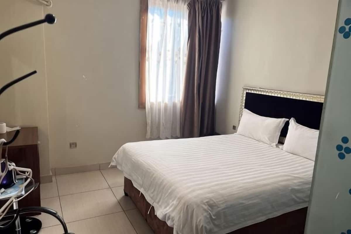 A bedroom with a bed, a window with curtains, a treadmill, and a wall with a blue pattern.