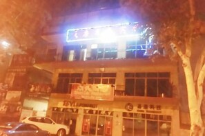 Un edificio con un letrero, un coche estacionado al frente y un árbol a la derecha.