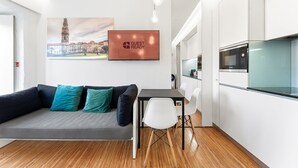 A modern living space with a sofa, a small dining table, and a kitchen area with appliances.