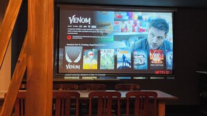 Eine Kinoleinwand zeigt einen Filmplakat für 'Venom', sowie weitere Filmtitel und Logos.