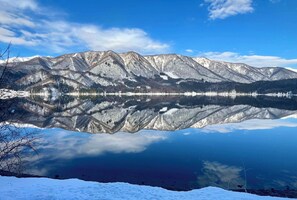 A mountain range reflected in a calm lake with snow-covered peaks and a clear sky. - Ember Lodge (Hakuba)