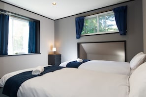 A hotel room with a large bed, a bedside table with a lamp, and a window with curtains. - Ember Lodge (Hakuba)