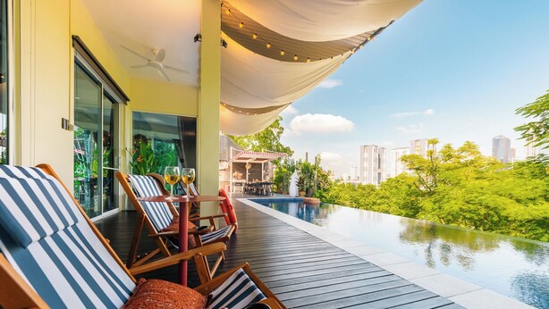 A rooftop infinity pool with lounge chairs and a canopy, overlooking a cityscape and lush greenery.