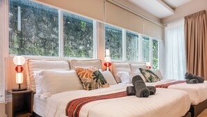 A hotel room with two beds, a nightstand, a lamp, and large windows with curtains.