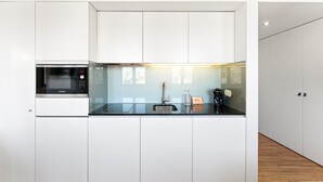 A modern kitchen with white cabinetry, a Bosch microwave, a coffee machine, and a sink. - GuestReady - Cathedral Design Apartments - Sé (Porto)