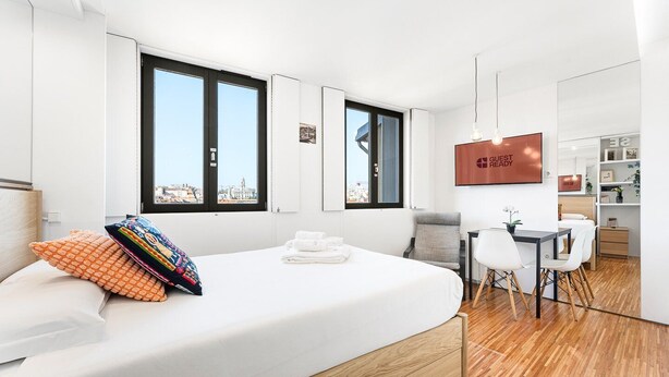 A modern hotel room with a large bed, a desk, and a view of the city. - GuestReady - Cathedral Design Apartments - Sé (Porto)