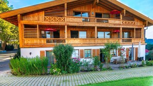 Un bâtiment en bois à deux étages, doté de balcons, d’un jardin aménagé et d’un banc.