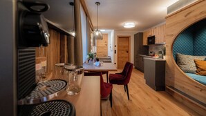 Une cuisine compacte avec des meubles en bois, un coin repas avec une table et des chaises, et un espace nuit aux lignes courbes avec un lit.