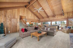 A spacious living area with a high ceiling and wooden walls, featuring a sofa, a coffee table, and a staircase leading to another level.