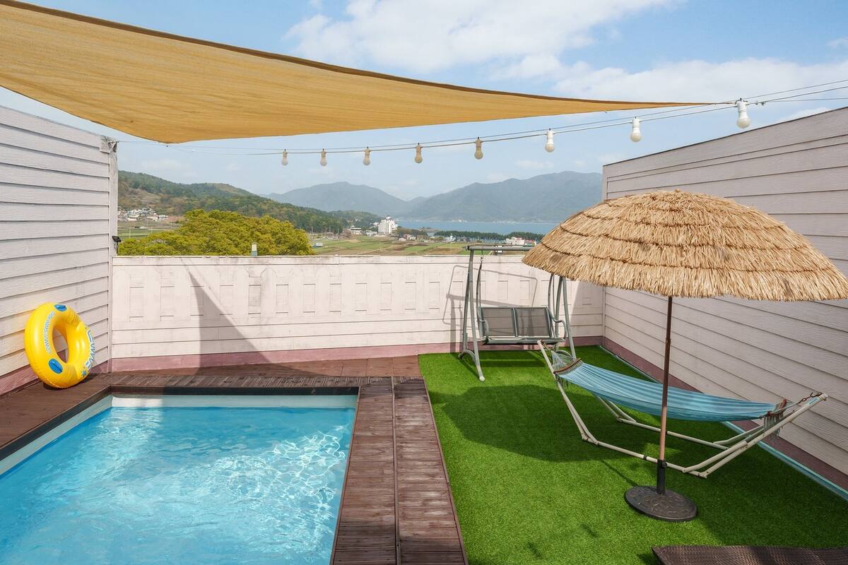 Ein Pool auf dem Dach mit Blick auf die Berge, eine Hängematte und ein Reetdachschirm.