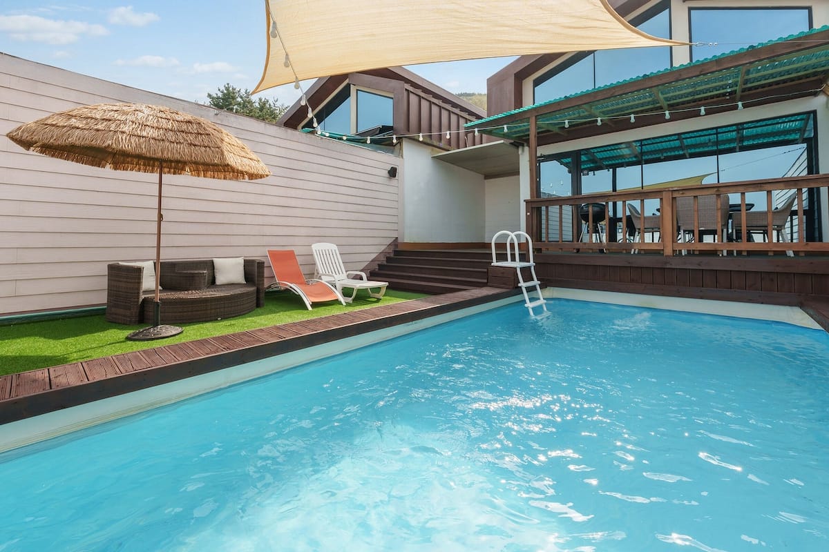 Ein Pool mit Holzterrasse, Liegestuhl und Strohdachschirm.