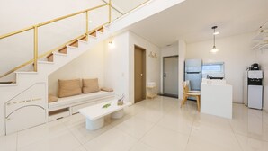 Een modern appartement met een trap, een zithoek met een bank en salontafel, een keuken met een koelkast en waterdispenser, en een deur naar een andere kamer.