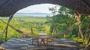 A hammock with a table and chairs on a checkered floor, overlooking a lush green landscape with a mountain in the distance. - Aldea Camalote (Aticama)