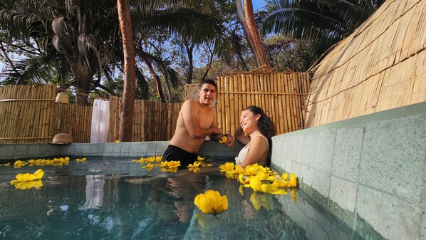 A pool with yellow flowers, bamboo walls, and palm trees. - Aldea Camalote (Aticama)