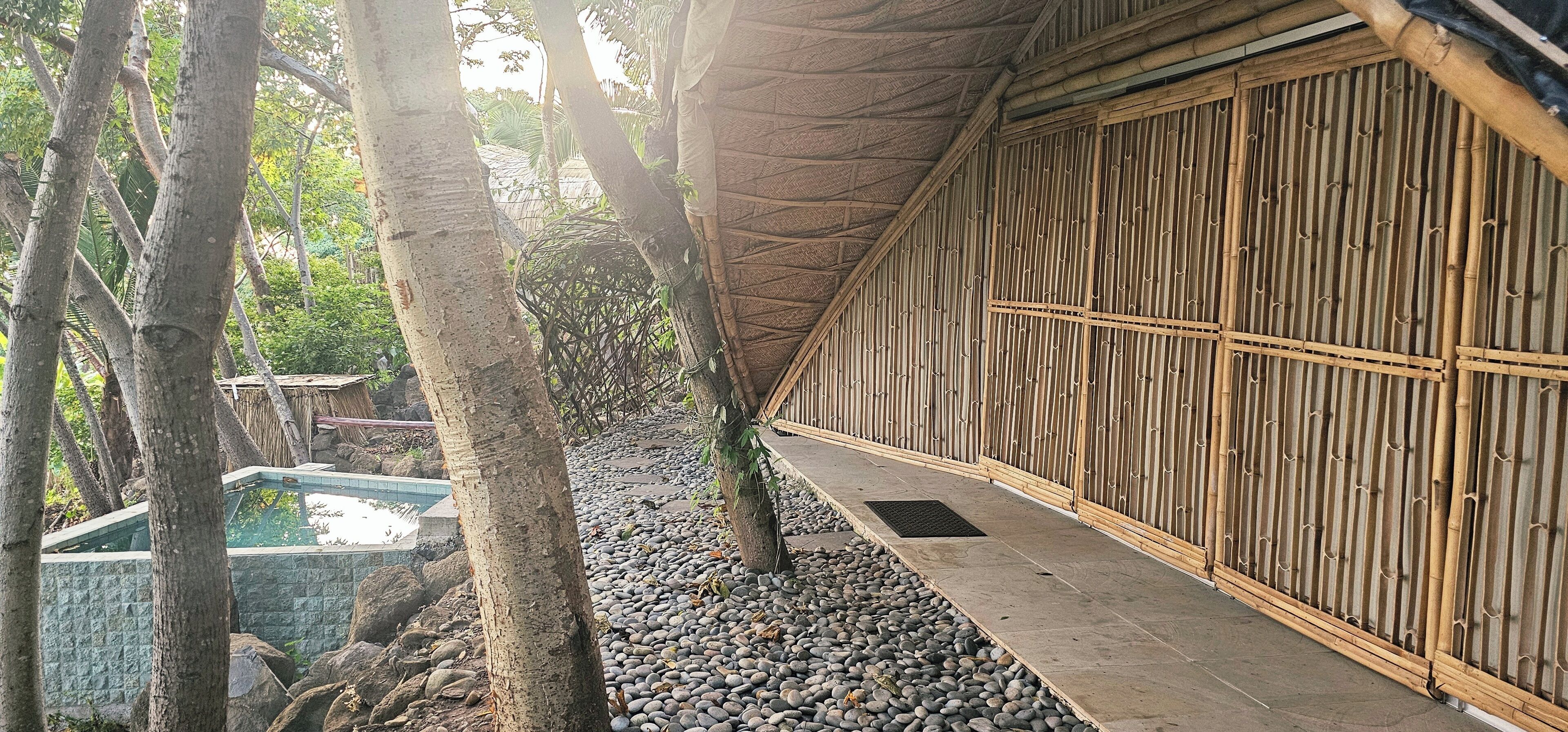 A traditional bamboo structure with a stone pathway and a small pool.