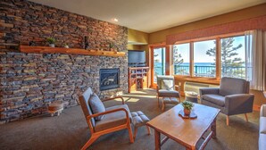 A cozy living room with a stone fireplace, comfortable seating, a television, and a view of the ocean. - Two Harbors Superior Lakefront 2BR | Pool | Hot Tub & Sauna | EV Charger (Two Harbors)