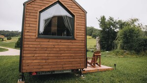 A small wooden cabin with a large window, a chair outside, and a grassy area. - Whispers of the Willow 1 by Tiny Away (Estramiac)