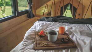 Una cama de madera con una bandeja de desayuno que incluye una taza, jugo y fruta cortada.