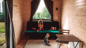 Interior acogedor de una cabaña con detalles de madera, un sofá verde, una mesita y una ventana con cortinas.