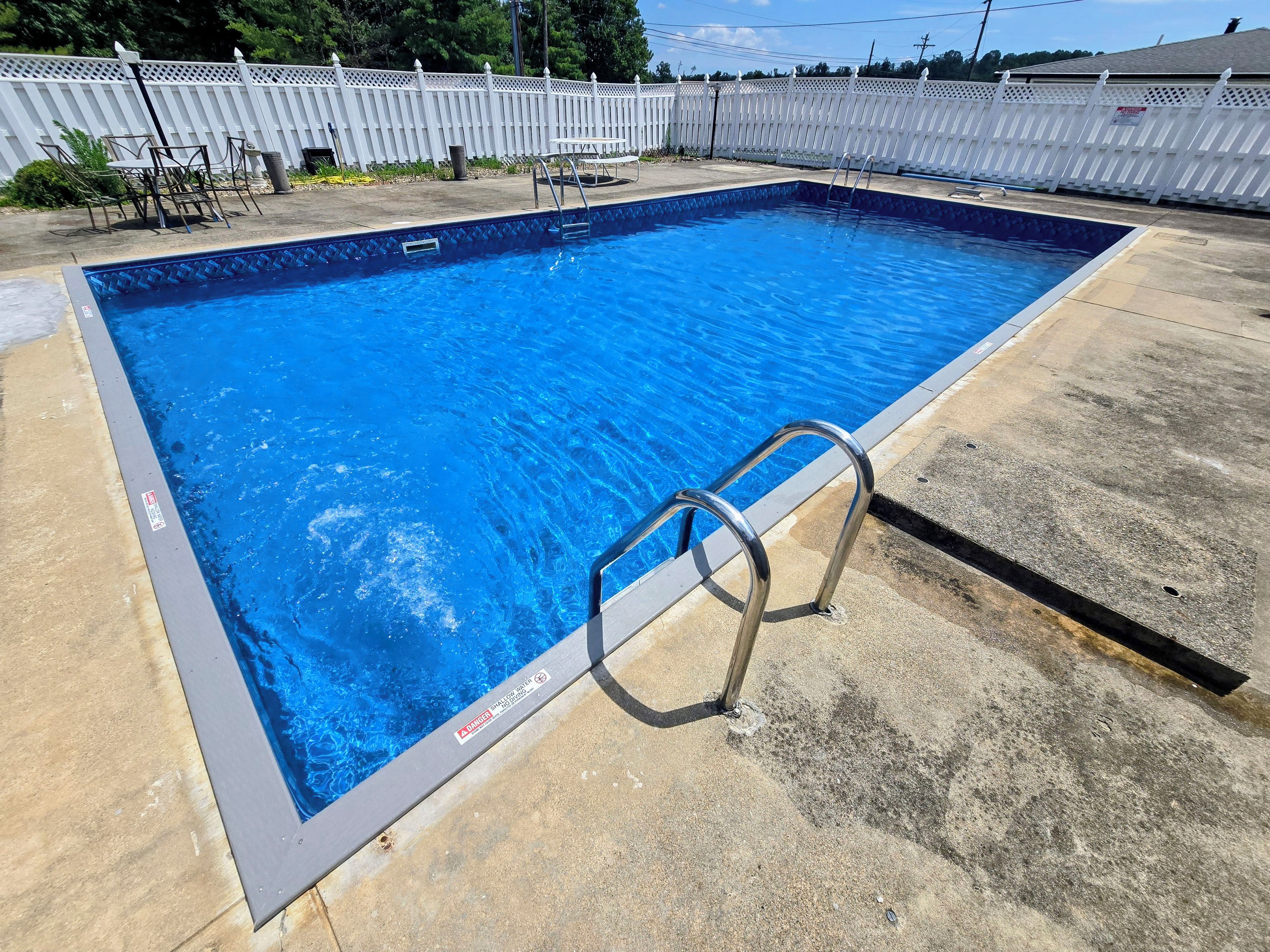 En rektangulær swimmingpool med en metalstige på den ene side, omgivet af et hvidt hegn.