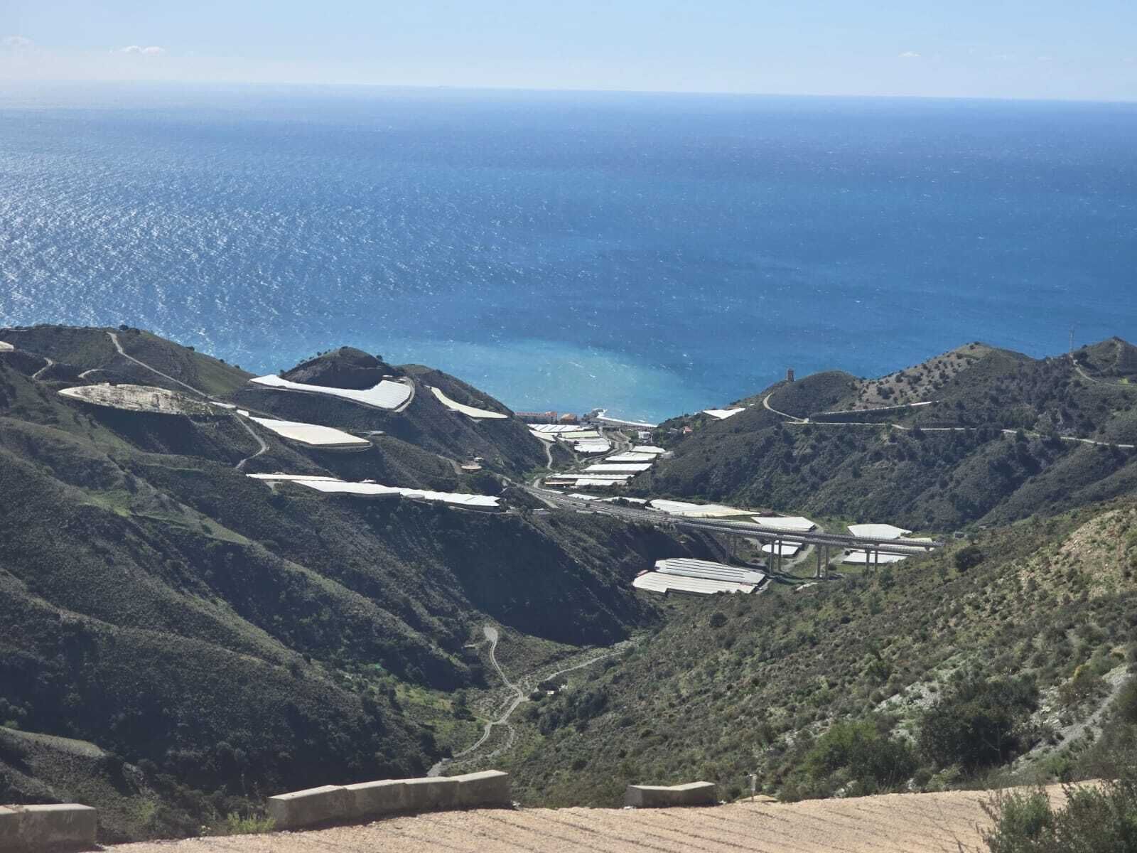 Paisaje montañoso con vista al mar, que incluye campos de cultivo en terrazas y un puente que une las zonas.