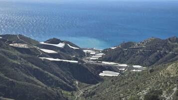 Paisaje montañoso con vista al mar, que incluye campos de cultivo en terrazas y un puente que une las zonas.