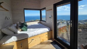 A bedroom with a bed, wooden walls, and large windows offering a view of the ocean.