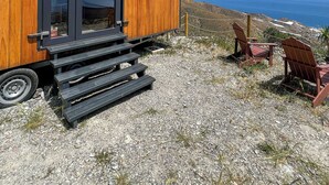 A modern wooden cabin with a large sliding door, a small window, and a set of stairs leading to a wooden deck.