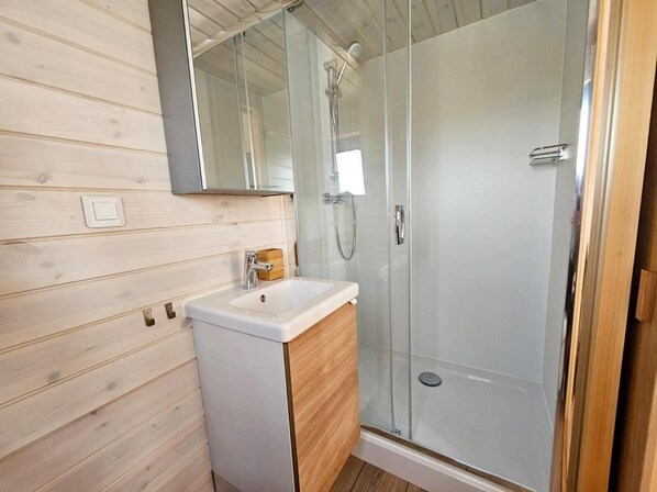 A modern bathroom with a wooden wall, a white sink, a mirror, and a glass-enclosed shower.