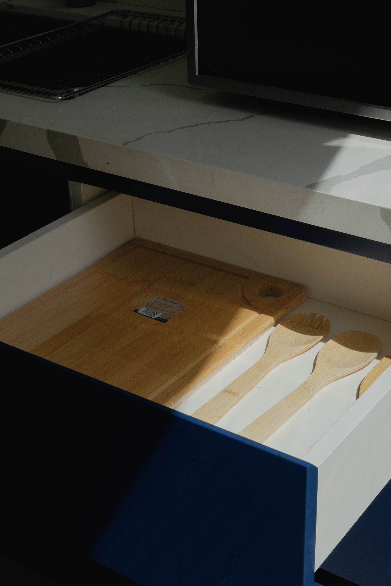 A drawer with a wooden cutting board, a spoon, and a fork.