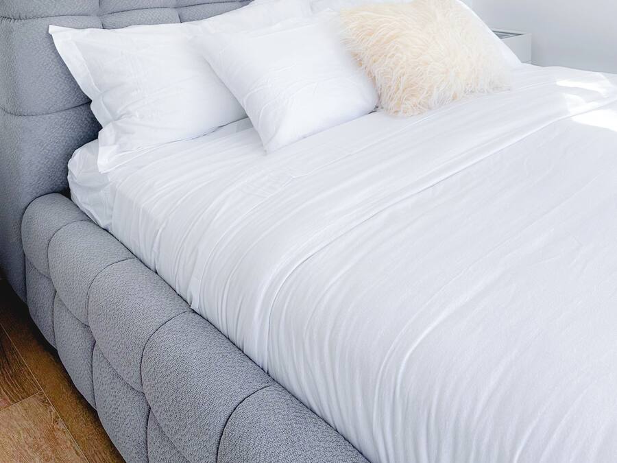 A bed with a grey upholstered headboard, white bedding, and a fluffy white pillow.